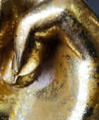 Close-up of a metallic gold object with a sculpted curved form and dark oxidized or patina details.
