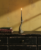 Decorative candlestick with a lit candle on a wooden surface against a yellow wall.