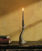 Decorative peacock-shaped candle holder with a lit candle on a wooden surface against a textured yellow wall.
