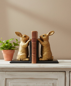 Two rabbit-shaped bookends on a wooden surface with a plant in the background.