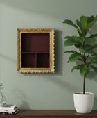 Decorative gold frame on a wall with a potted plant and books on a shelf below.