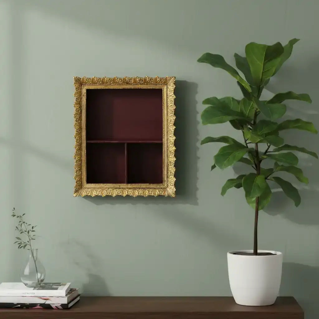 Decorative gold frame on a wall with a potted plant and books on a shelf below.