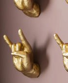 Gold hand gestures making the 'rock on' sign against a pink background