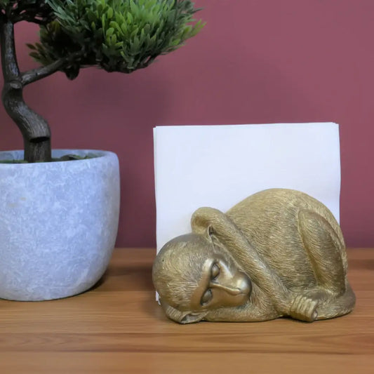 Gold monkey figurine on a wooden surface with a plant and white candle in the background.