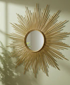 Decorative gold sunburst mirror on a wall with candles and books in the corner.
