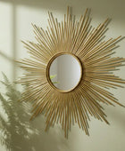 Decorative gold sunburst mirror on a wall with a plant shadow.
