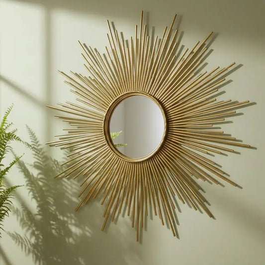 Decorative gold sunburst mirror on a wall with a plant shadow.