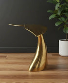 Gold side table on a wooden floor with a dark wall and plant in the background