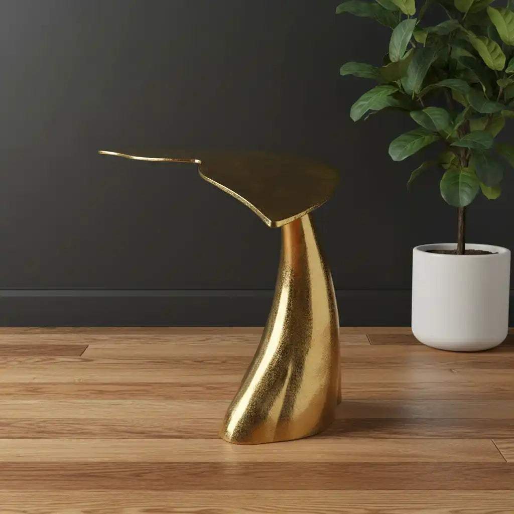 Gold side table on a wooden floor with a dark wall and plant in the background