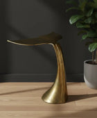 Gold leaf-shaped stool on a wooden floor with a dark wall and potted plant in the background