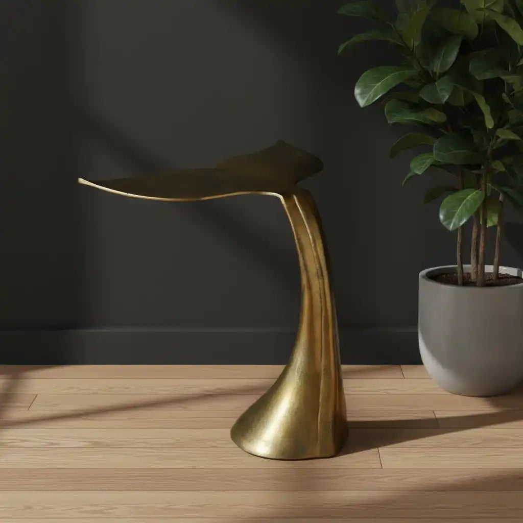 Gold leaf-shaped stool on a wooden floor with a dark wall and potted plant in the background