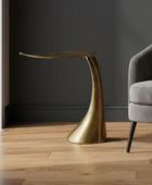 Gray armchair with cushions next to a gold side table in a room with dark walls and wooden floor.