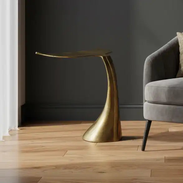 Gray armchair with cushions next to a gold side table in a room with dark walls and wooden floor.