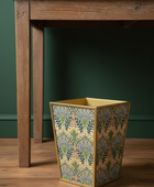 Decorative trash can with floral pattern on a wooden table against a green wall.