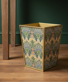 Decorative waste bin with floral pattern on a wooden floor against a green wall