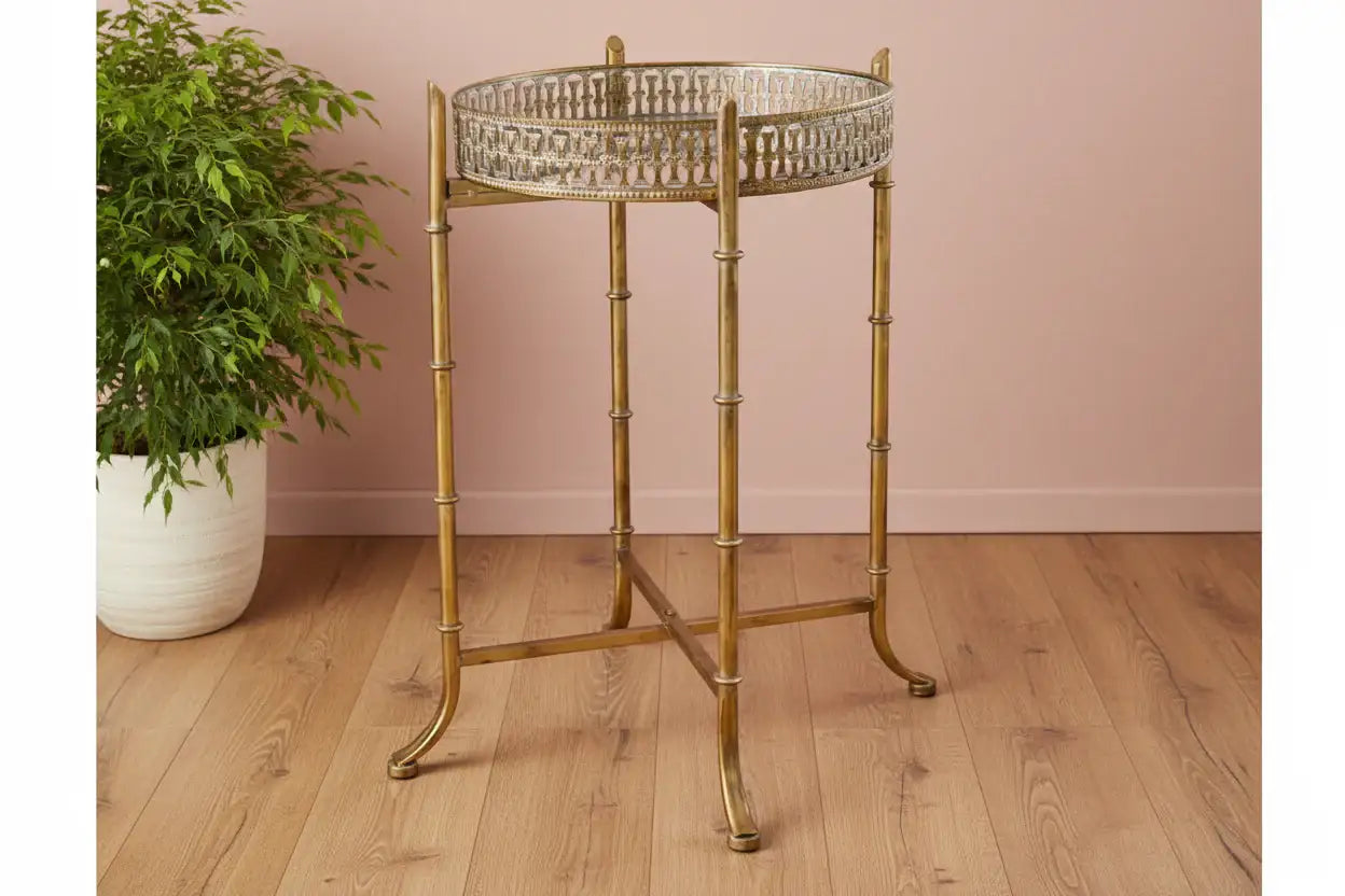 Gold side table with decorative tray on a wooden floor against a pink wall
