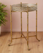 Decorative brass side table with a glass top on a wooden floor against a pink wall.