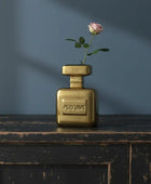 Gold perfume bottle with a pink rose on a dark wooden surface against a blue wall