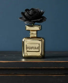 Gold perfume bottle with a black rose on top against a blue background