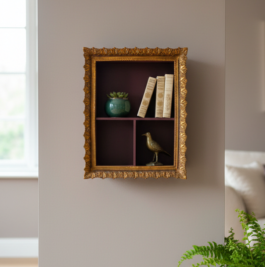 Decorative wall shelf with gold frame containing books, a bird figurine, and a green vase.