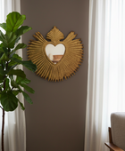 Decorative heart-shaped mirror on a wall with a plant and chair in the background