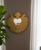 Decorative wall mirror with heart design on a brown wall, next to a plant and window.