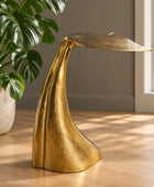 A gold metal whale tail sculpture serving as a table lamp, styled on a woven mat with potted plants in the background.