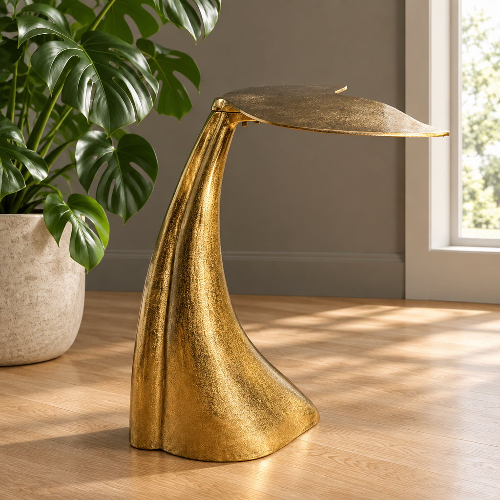A gold metal whale tail sculpture serving as a table lamp, styled on a woven mat with potted plants in the background.