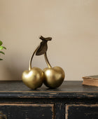 Decorative gold cherries on a wooden surface with a plant in the background