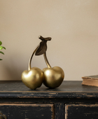 Gold cherry figurine on a wooden surface with a plant and book in the background