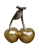 Bronze sculpture of two cherries on a wooden surface with a gray background