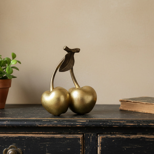 Gold cherry figurine on a wooden surface with a plant and book in the background