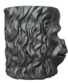 Black sculpture of a face with wavy hair on a wooden surface