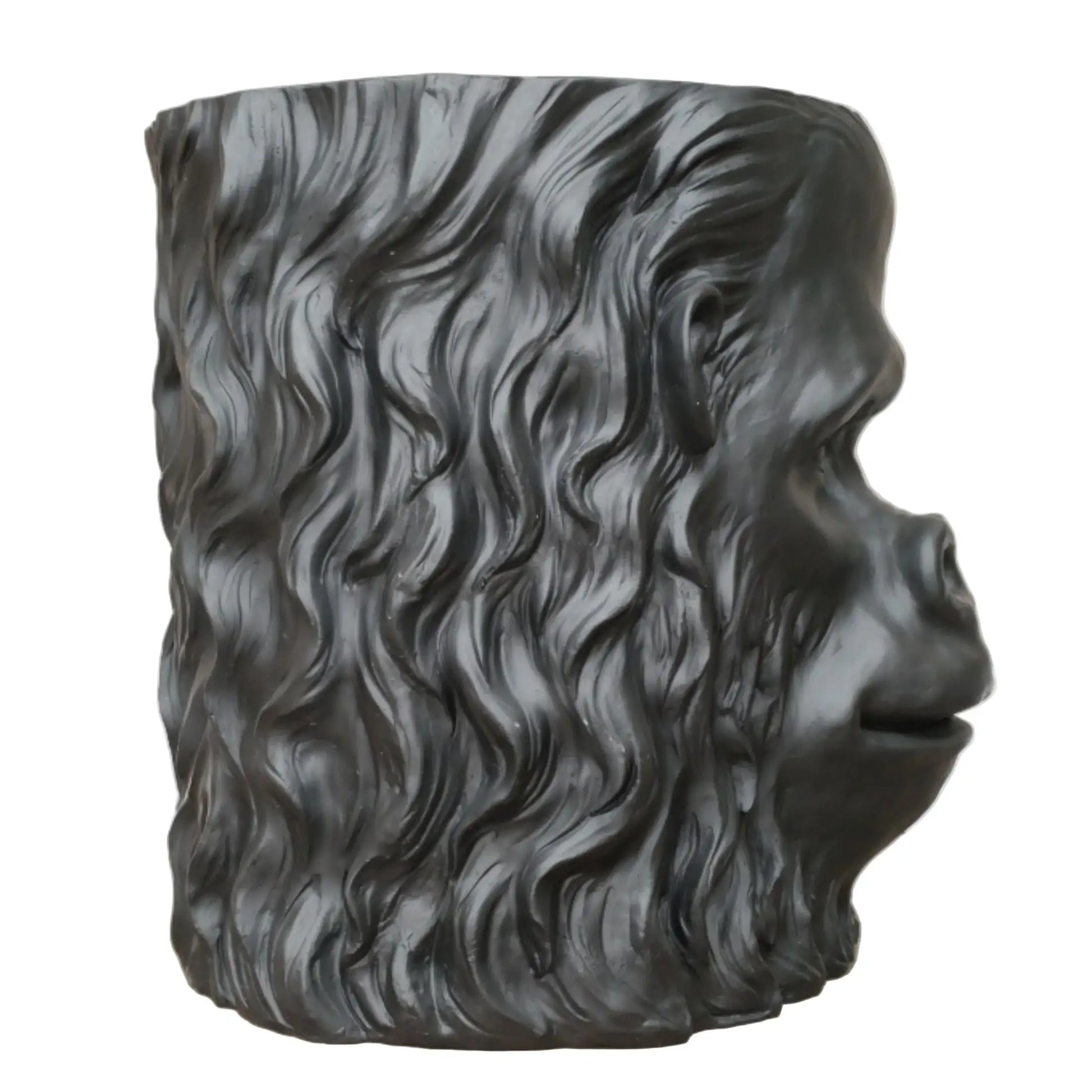 Black sculpture of a face with wavy hair on a wooden surface
