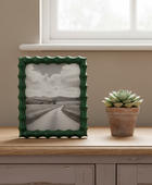 Green textured picture frame with a black and white photo on a wooden surface next to a potted succulent.