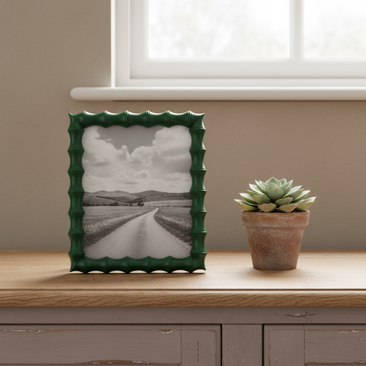 Green textured picture frame with a black and white photo on a wooden surface next to a potted succulent.