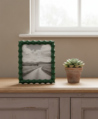 Green-framed picture on a wooden surface with a potted plant