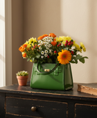 Green handbag filled with flowers on a wooden surface near a window.