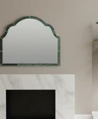 Decorative mirror with green frame on a beige wall above a white fireplace.