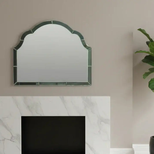 Decorative mirror with green frame on a beige wall above a white fireplace.
