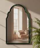 Arched mirror with green frame on a wall with a plant in the foreground