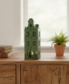 Green house-shaped lantern on a wooden surface with books and a potted plant.