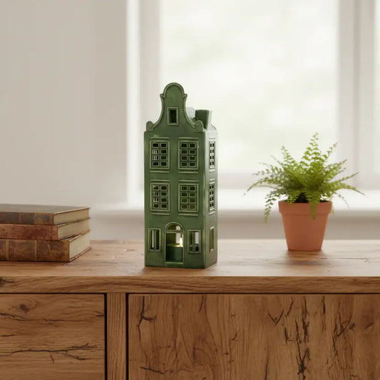 Green house-shaped lantern on a wooden surface with books and a potted plant.