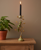 Decorative candle holder with a lit candle on a wooden surface next to a plant.