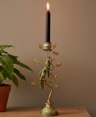 Decorative candle holder with birds holding a candle next to a potted plant on a wooden surface.