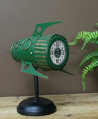 Green clock design on a stand with a plant in the background