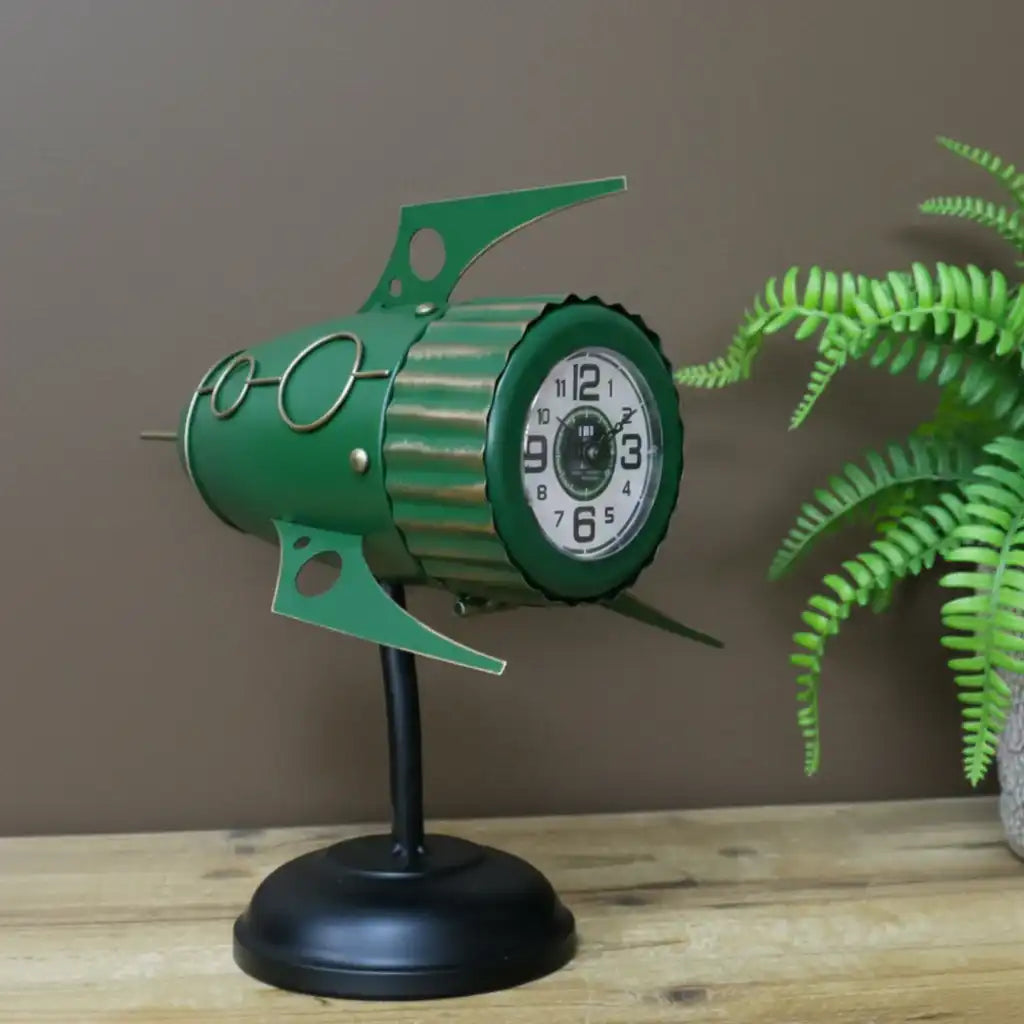 Green clock design on a stand with a plant in the background