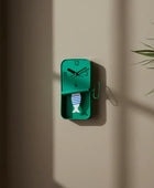 Green wall clock on a beige wall with a plant to the right