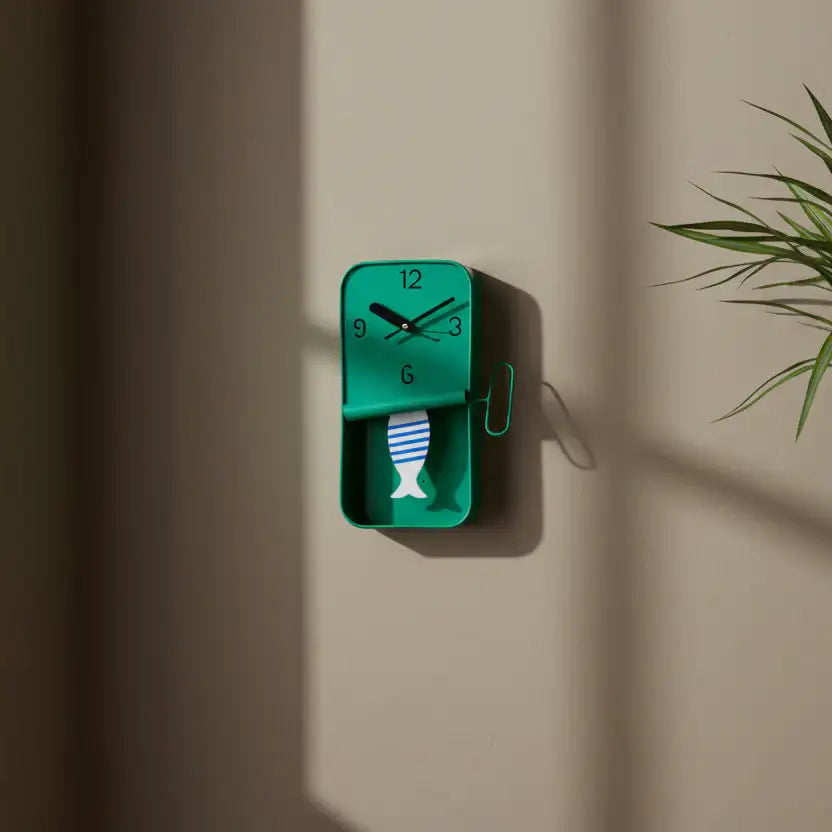 Green wall clock with fish design on a beige wall