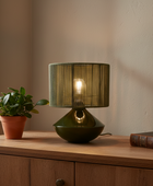 Green table lamp on a wooden surface with a plant and book in the background